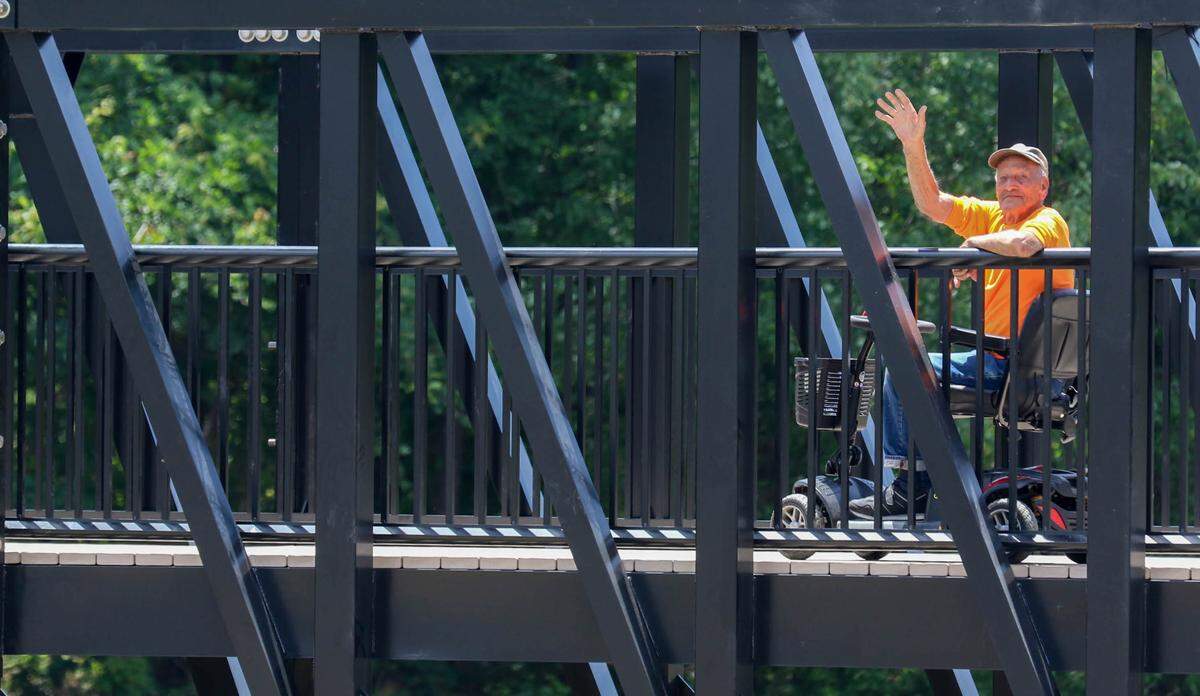 Jim Farnham waves from the new pedestrian bridge over the new dam at Gibson Pond Park in Lexington. Farnham has watched the construction daily for about a year.