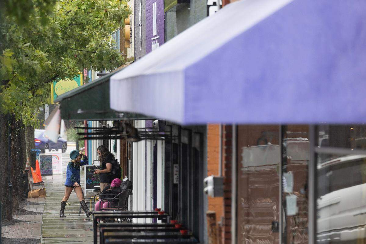 People walk through rain and past a pile of barricades in Five Points before Tropical Storm Debby arrives in Columbia, South Carolina on Tuesday, August 6, 2024.