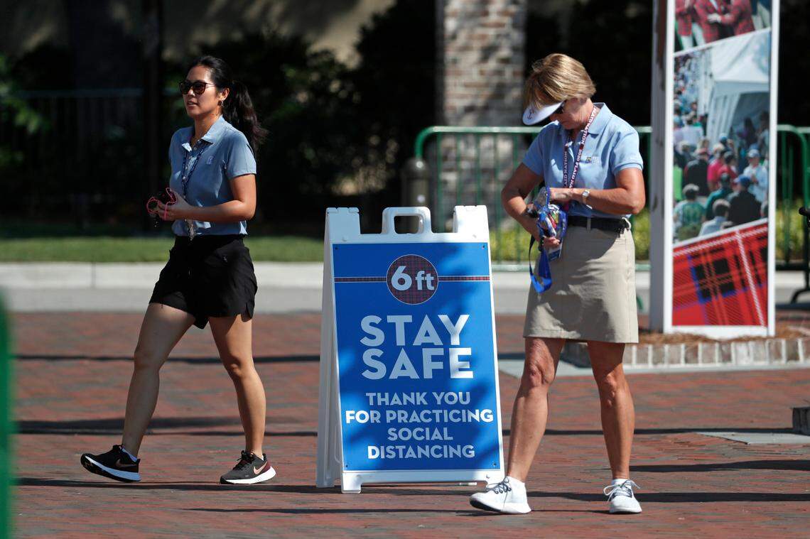 Volunteers walk past a sign reminding people of social distancing practices during the third round of the RBC Heritage golf tournament, Saturday, June 20, 2020, in Hilton Head Island, S.C. (AP Photo/Gerry Broome)
