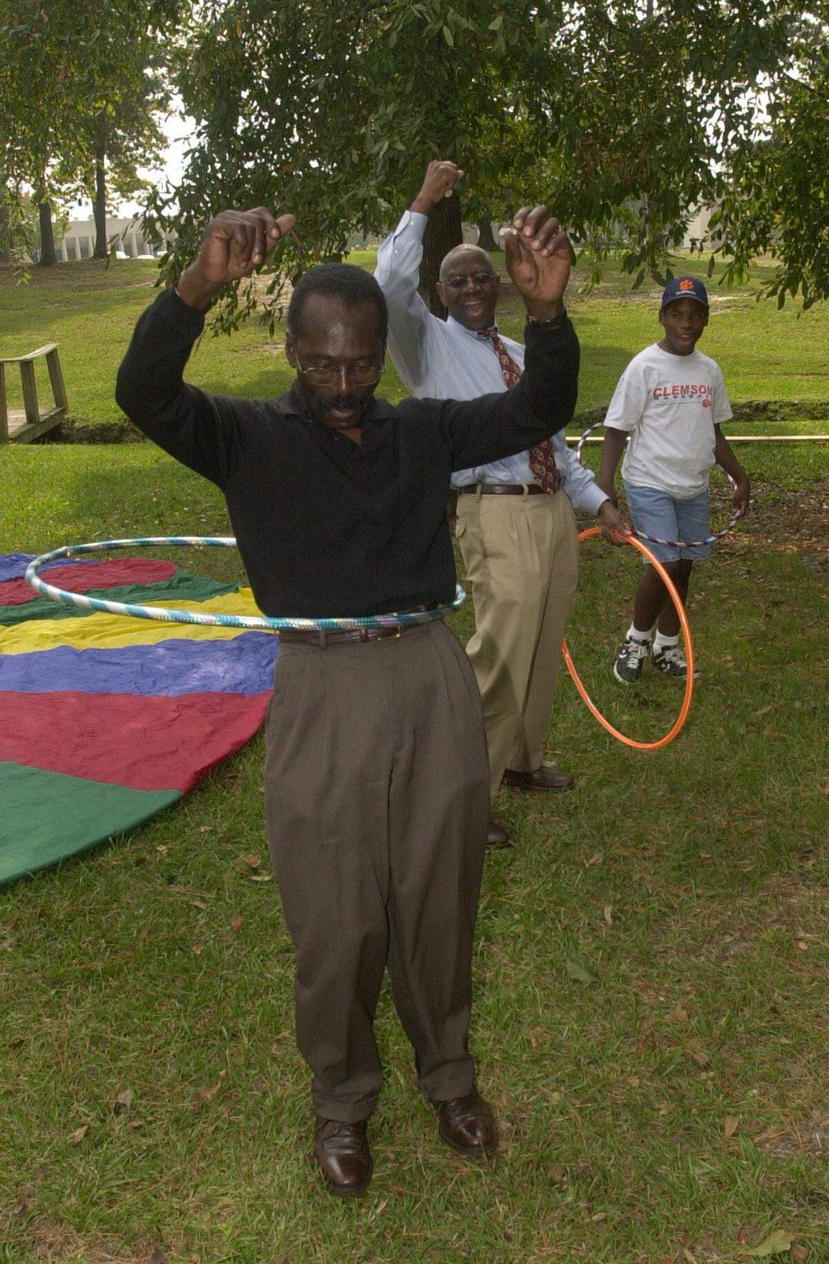 Columbia, SC, Richland County Councilman Paul Livingston,center, cheers on City of Columbia Councilman Sam Davis as he proves he has not lost his ability to hula-hoop. A city parks and recreation booth was set up to encourage people to play in honor of World Wide day of Play, at the Eau Claire Renaissace Faire.