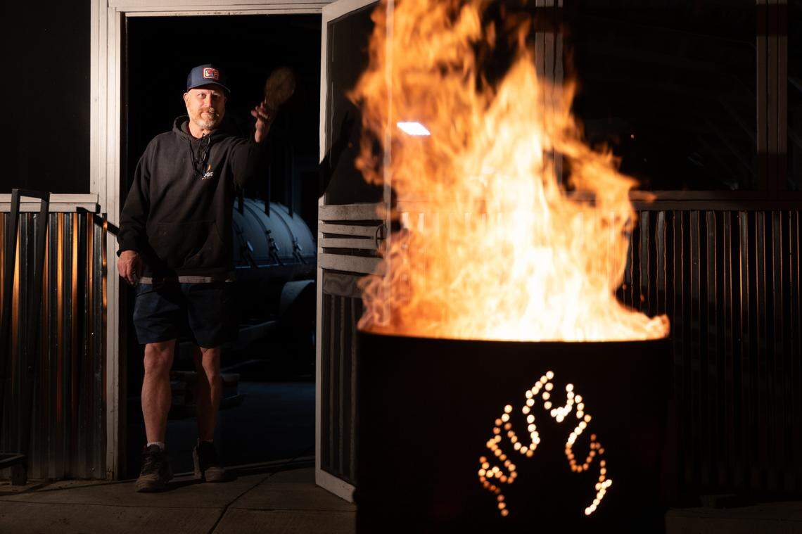 Robbie Robinson, owner of City Limits Barbeque in West Columbia, tosses a log into a burn barrel on Friday, March 28, 2025.