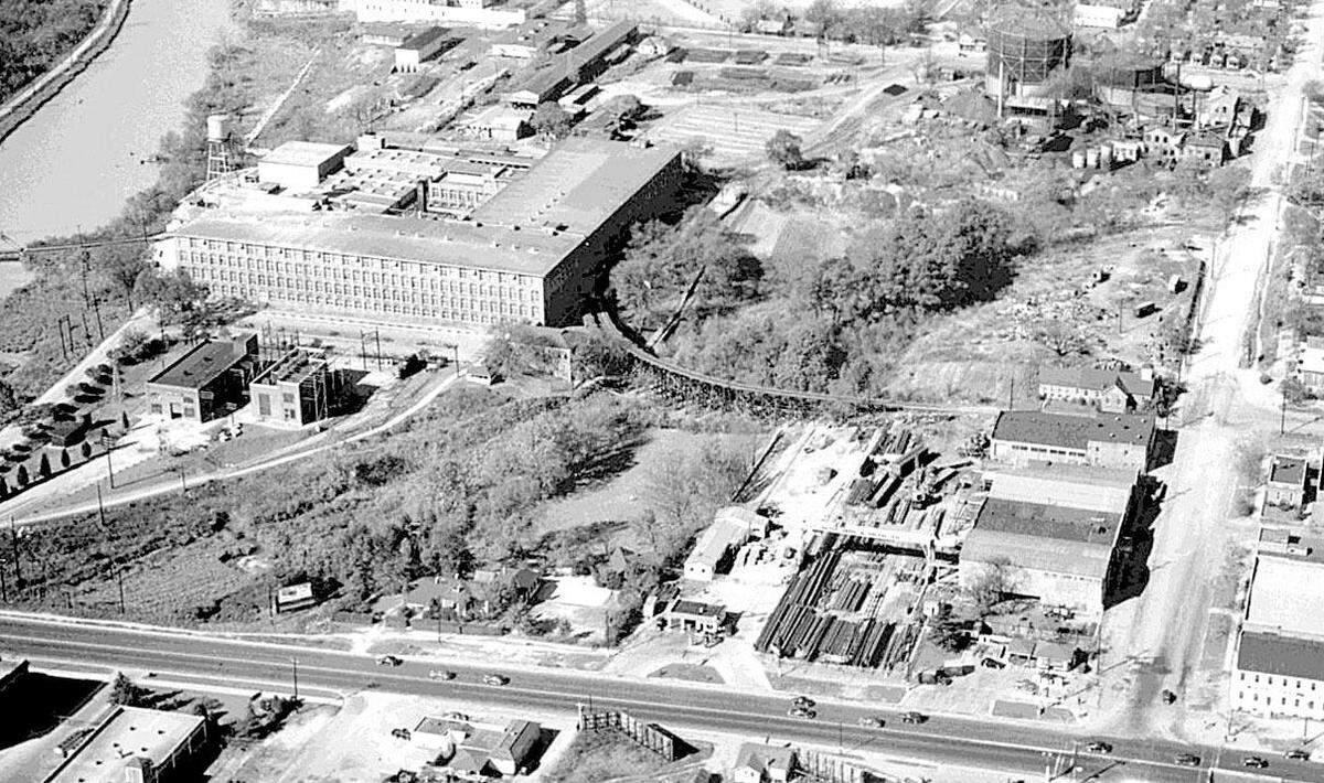 An aerial photograph from the 1940s shows a dirt Huger Street intersecting with the paved Gervais Street. SCE&G’s gas manufacturing plant is on the left side of Huger at top right; Kline Iron & Steel Co. is below it, fronting on Gervais; and the Columbia Mill, left lower on the canal, is now the State Museum.