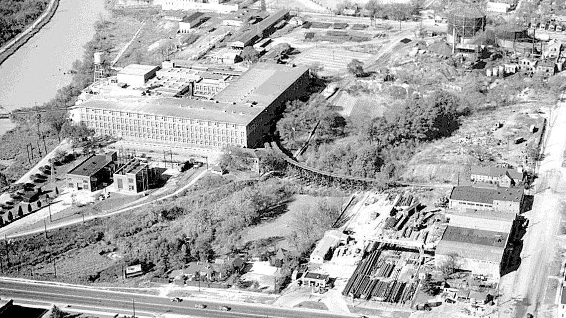 An aerial photograph from the 1940s shows a dirt Huger Street intersecting with the paved Gervais Street. SCE&G’s gas manufacturing plant is on the left side of Huger at top right; Kline Iron & Steel Co. is below it, fronting on Gervais; and the Columbia Mill, left lower on the canal, is now the State Museum.