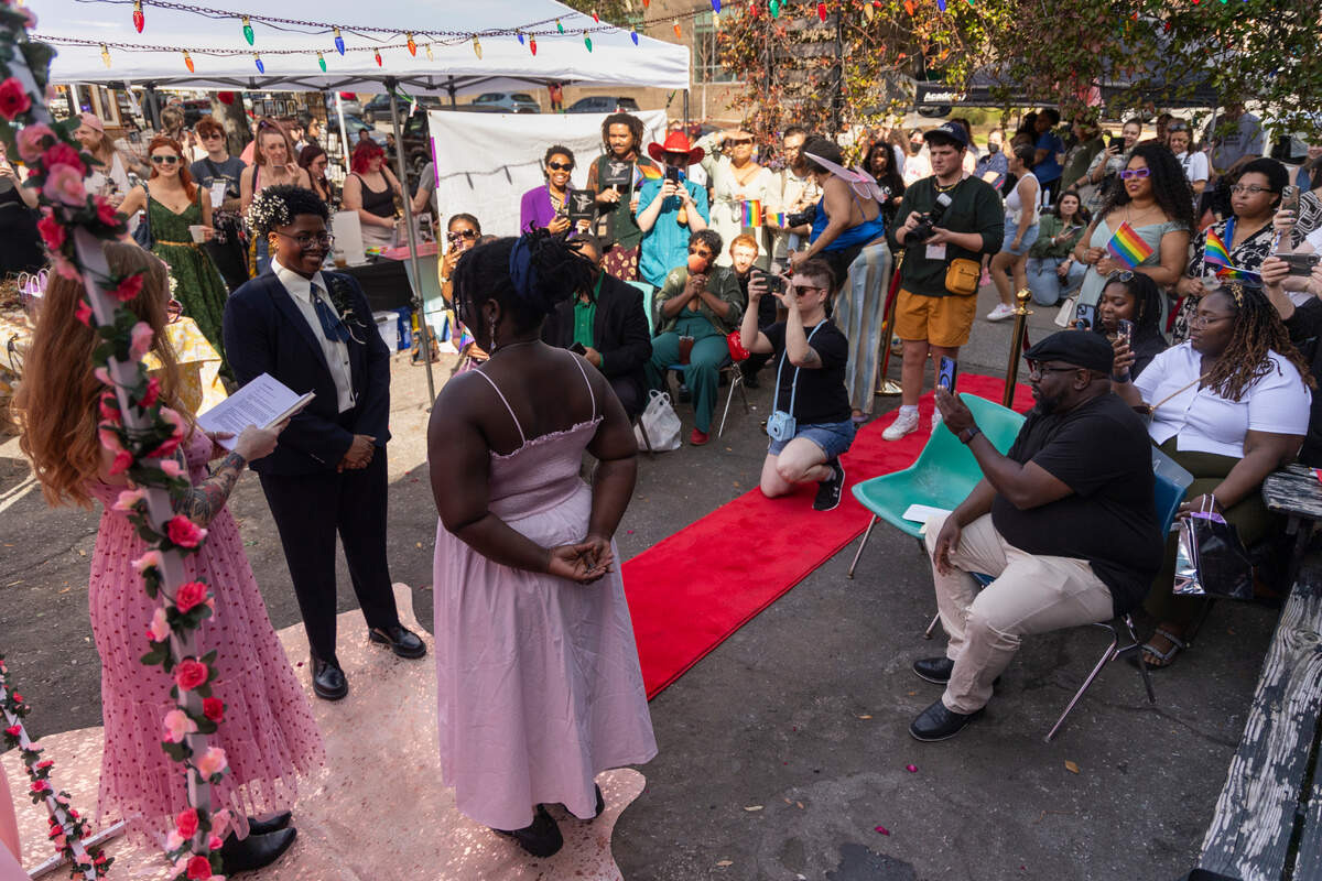 Friends, family and art market attendees watch as Mahkia Greene and Klo Hampton marry at Y’all-Mart, a quarterly art fair series, at Art Bar in Columbia, South Carolina on Sunday, February 9, 2025. Wedding officiant and Y’all-Mart cofounder spoke of the importance of love as an act of resistance in her service, and asked those in attendance to show solidarity with the newly married couples.