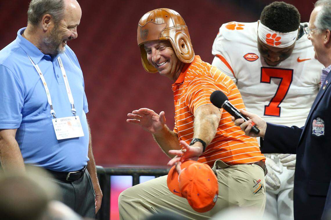 Clemson Tigers head coach Dabo Swinney celebrates with the old leather helmet (awarded to the winner of the now-Aflac Kickoff Game) after a win against Georgia Tech in 2022. Peach Bowl CEO/president Gary Stokan is to his left.
