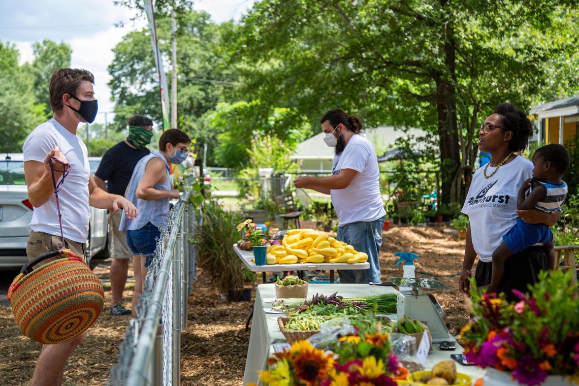 April Jones holds her son Edward Brown, 2, and speaks to costumers in her front yard during the Pinehurst Farmers Market on Wednesday, July 22, 2020. She hosts the farmers market in her front yard on Wednesdays to help her neighbors have access to quality food.