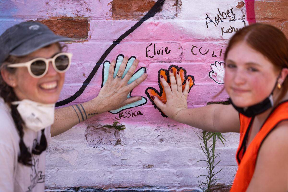 Jessica Bornick, widow to Aaron Graves and member of Those Lavender Whales, and their daughter pose with their painted handprints on the mural on South Main Street in Columbia, South Carolina on Saturday, June 28, 2025. The building and mural were deconstructed after it was purchased by the USC Development Foundation. 