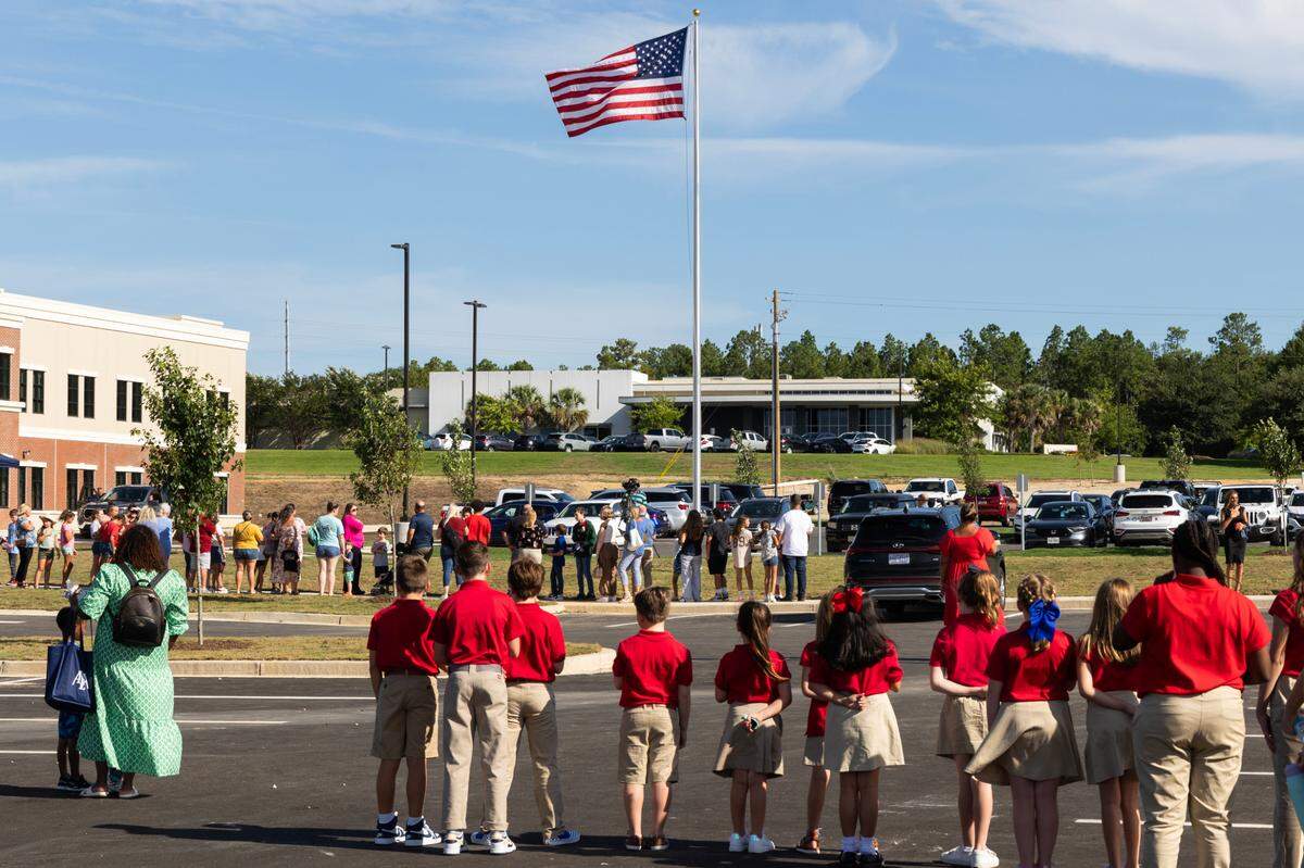 Students and families stand for the Pledge of Allegiance during a grand opening ceremony at the new American Leadership Academy in Lexington on Thursday, August 10, 2023.