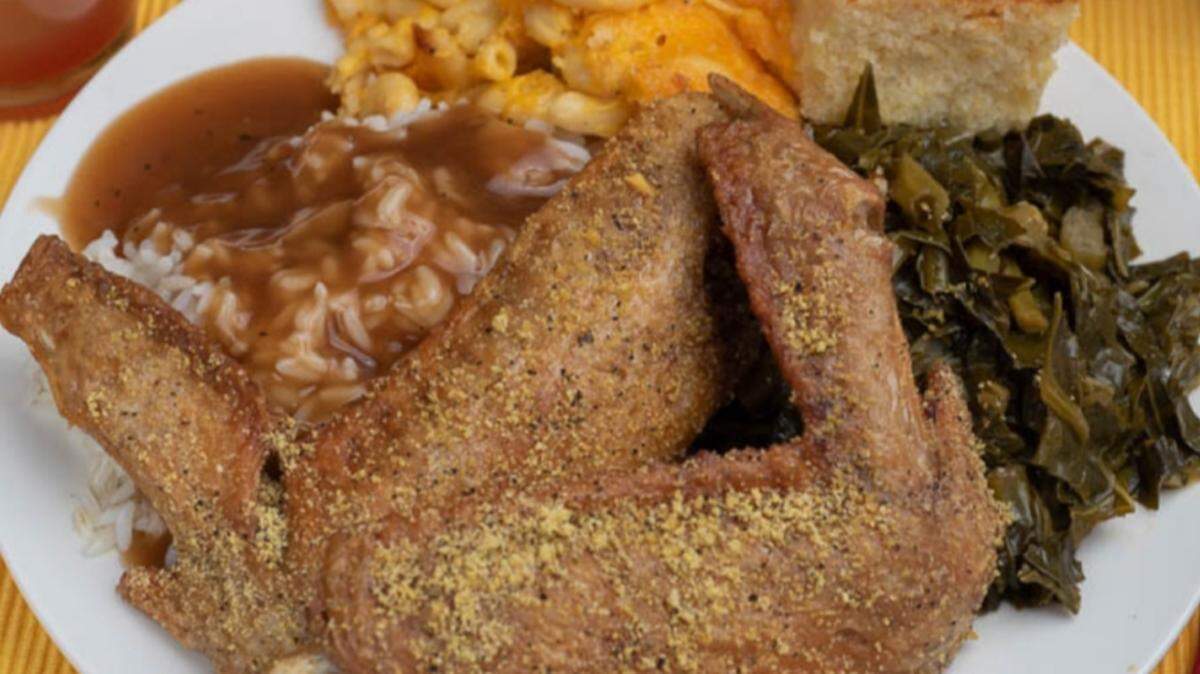 A plate of comfort soul food that includes lemon pepper fried turkey wings, with collard greens, macaroni and cheese, corn bread and rice and gravy.