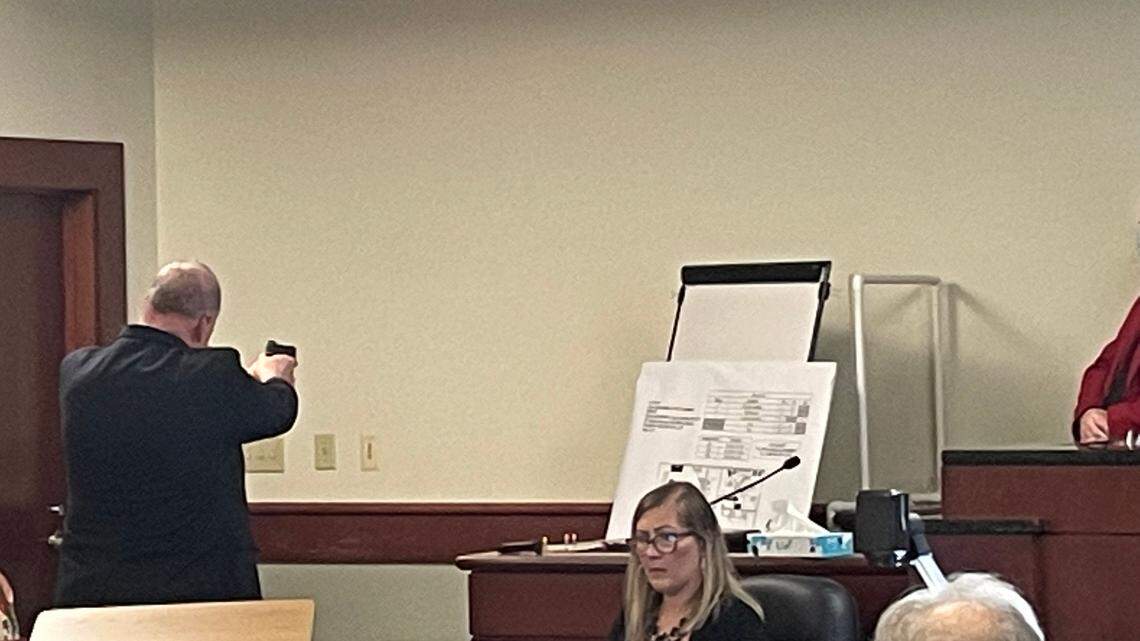 Charles Mills, a gun expert with FN manufacturer, aims an unloaded gun before pulling the trigger in the case of Adam Lazzarini, a doctor accused of shooting a man.