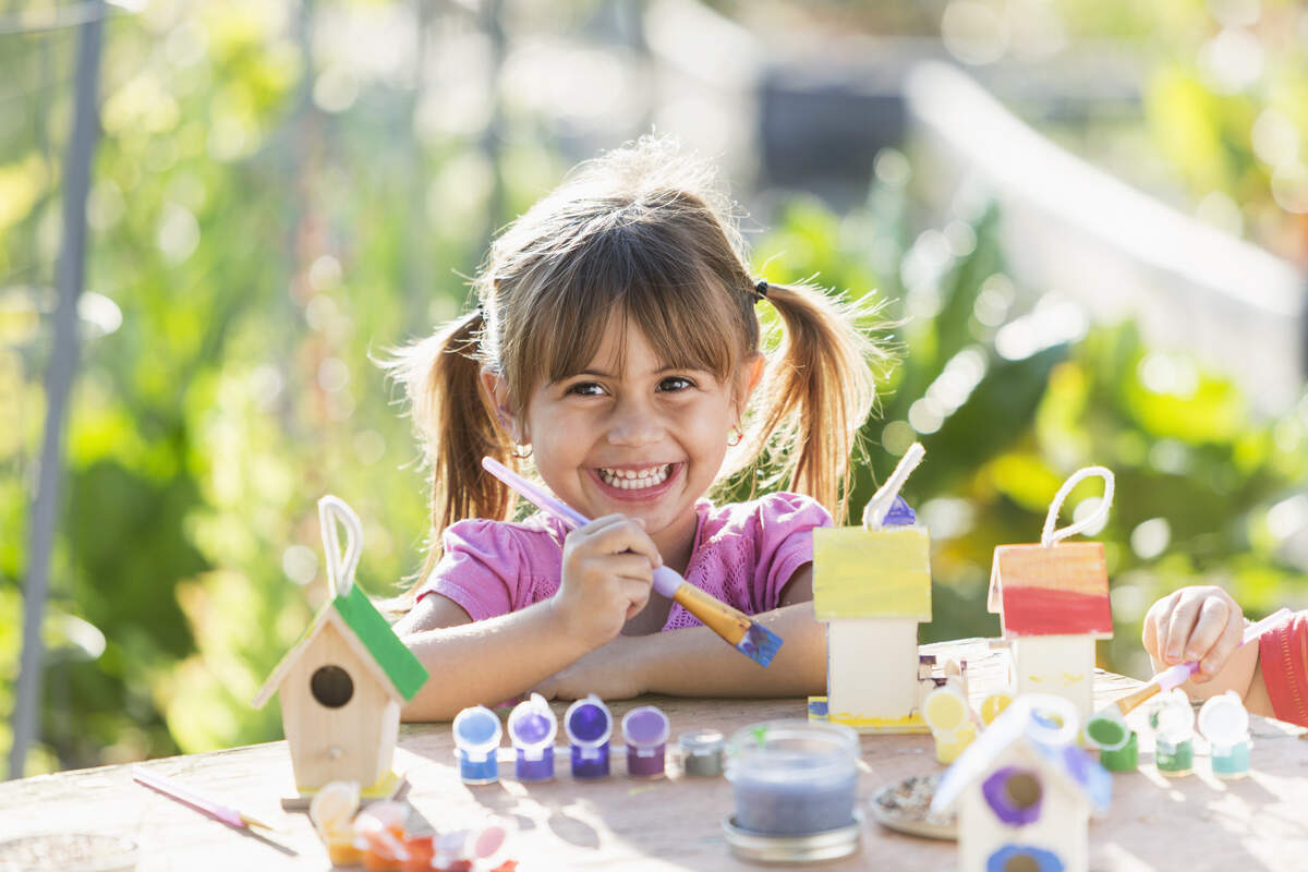 Little girl (3 years, Hispanic) painting little wooden bird feeder.