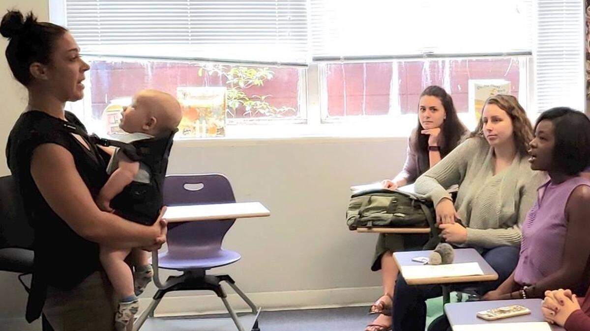 Columbia College professor Dr. Amanda Stefanski instructs her class while holding a student’s baby in a chest carrier.