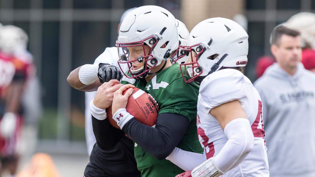 South Carolina quarterback Spencer Rattler carries two balls as DeAngelo Gibbs (17) and Joseph Byrnes (43) try to punch them out during the Gamecocks’ practice in Columbia on Thursday, March 23, 2023.