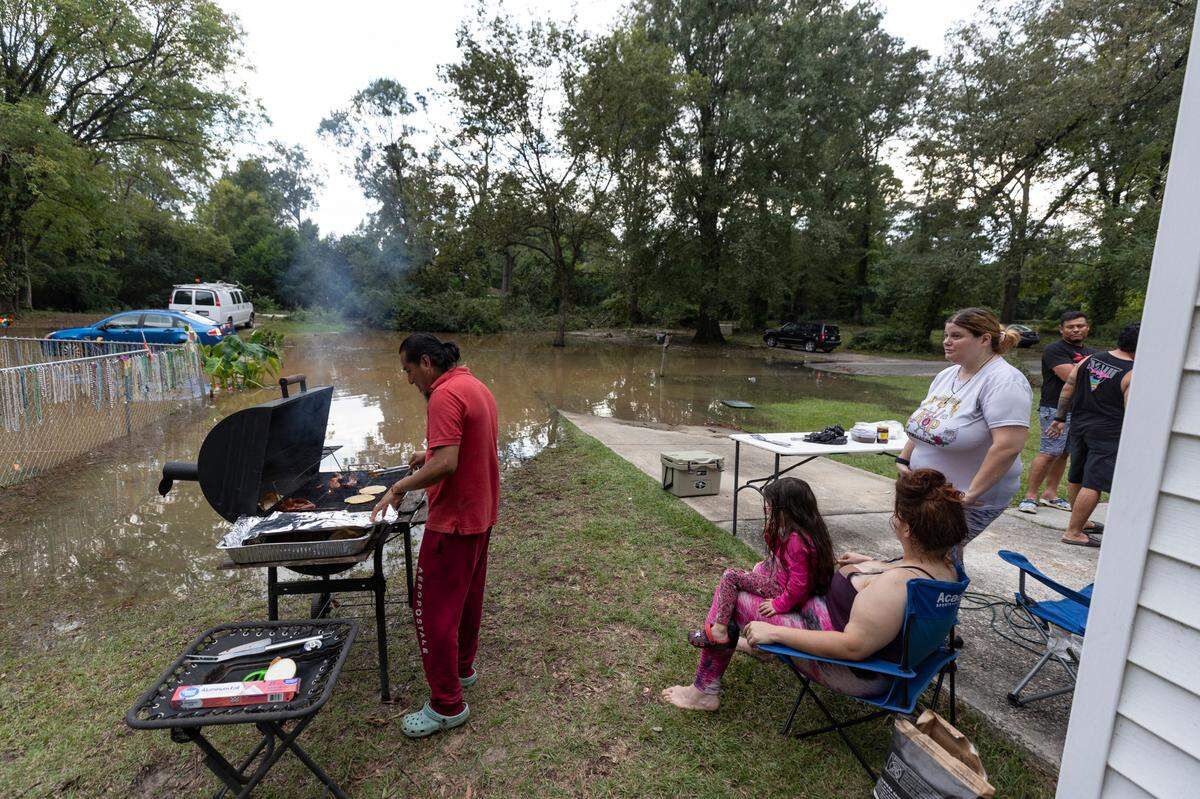 Chris Gonzalez prepares dinner in a high spot in his neighbor’s yard on Hudson Avenue as flood waters creep into the Riverland Park subdivision in Cayce on Sunday, Sept 29, 2024. Gonzalez and his wife, Tiffany Este, right, her sister Amanda Este, seated, daughter Sophia Gonzales, 4 and mother-in-law were encouraged to evacuate but are unable to because of their four pets.