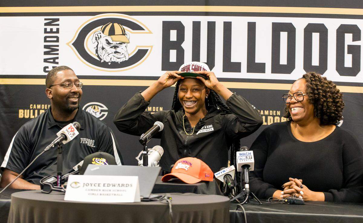 Camden High School basketball player Joyce Edwards puts on a Gamecocks hat, indicating her choice to play at the University of South Carolina over Clemson and LSU. Seated with her are her parents Rasheedah and Charlie Edwards.