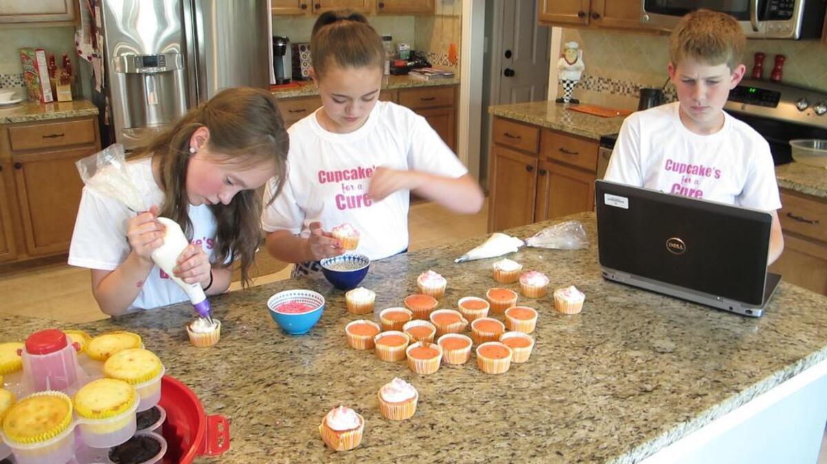 Pleasant Hill Elementary School students Katelyn Reneau (left) and Mattie Lambrecht decorate cupcakes for Cupcakes for a Cure’s sale at Pleasant Hill Middle School on Thursday. Business manager Charlie Winston looks on.
