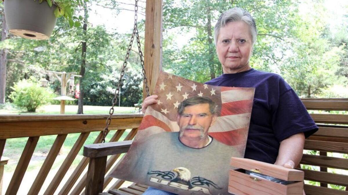 Myra Montgomery Ansell holds a photo of her husband, Charlie, and the ashes of her dog, Bella, on the front porch of her home where her husband was killed in an accident last year.
