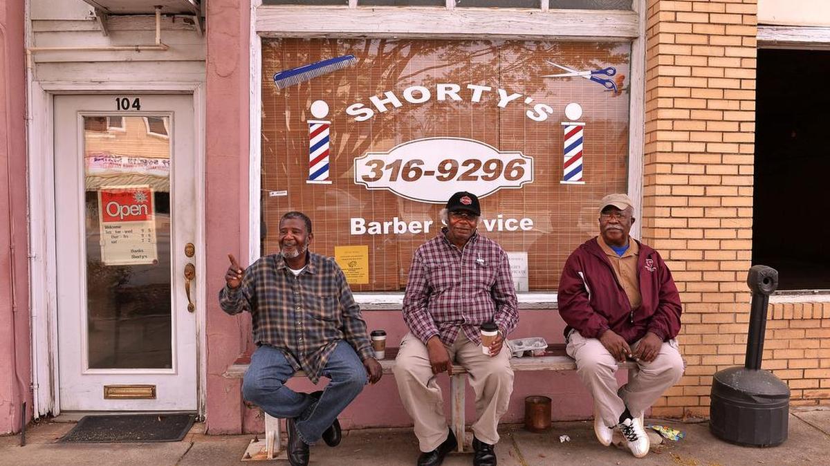 Joe Suber, left, waving at a passerby, sits and chats with friends Eugene Thompson, center, and John Gilliam, right, on Main Street in downtown Woodruff last week. Suber is the owner of Shorty's Barber Service.