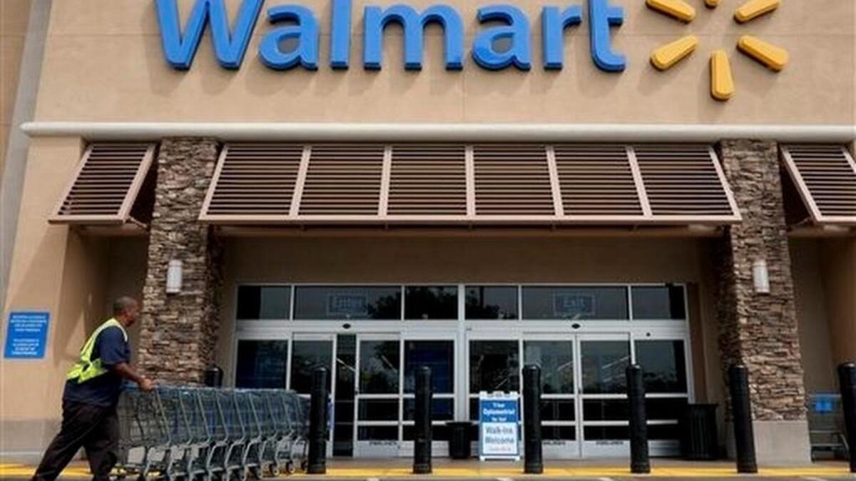 FILE - In this May 9, 2013 file photo, a worker pushes shopping carts in front of a Wal-Mart.