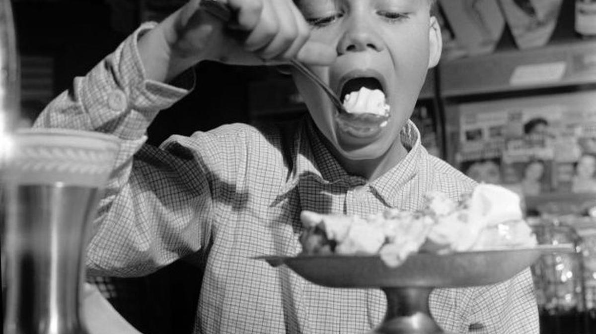Circa 1950: A young boy eats a large spoonful of ice cream.