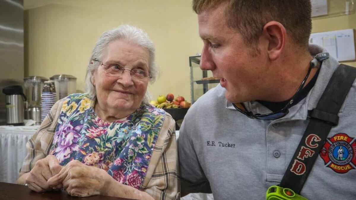 
Christine Moore reunites Monday morning with her hero, Columbia firefighter Ethan Tucker. Two months ago Tucker forced in the door to 91-year-old Moore’s apartment on the third floor of the Forest Pines retirement community and scooped her up from her bed and carried her over his shoulder to safety. A three-alarm fire was blazing, and Moore, who can’t walk, couldn’t escape. Since then, a number of the Forest Pines residents have been living in the Comfort Inn along Bush River road. On Monday, the hotel held a breakfast for the first responders who helped the home’s residents on the day of the fire.
