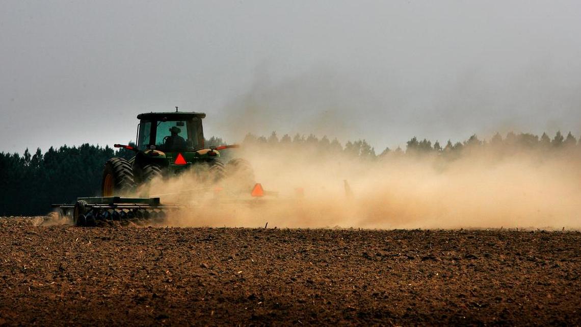A Walter P. Rawl & Sons worker kicks up a cloud of dust as he plows a field.