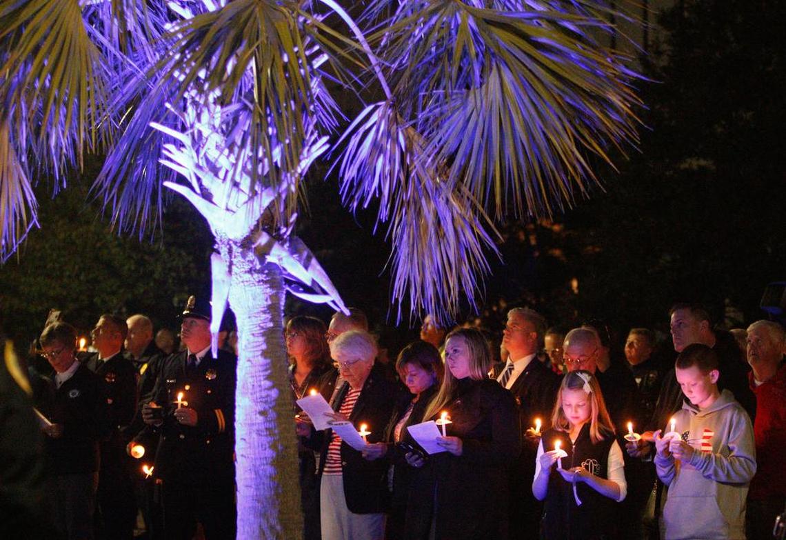 A palmetto tree lit in blue glows above people paying their respects during the Law Enforcement Memorial Service on the South Carolina State House grounds on Friday.