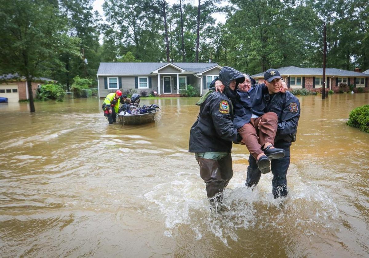 In this Oct. 5, 2015, photograph, DNR officer Brett Irvin and Lexington County Deputy Dan Rusinyak carry June Loch to dry land after she was rescued from her home in the Pine Glen subdivision off of Tram road in the St. Andrews area of Columbia. Some residents had to abandon their homes because of flooding coinciding with release of water from the Lake Murray dam.