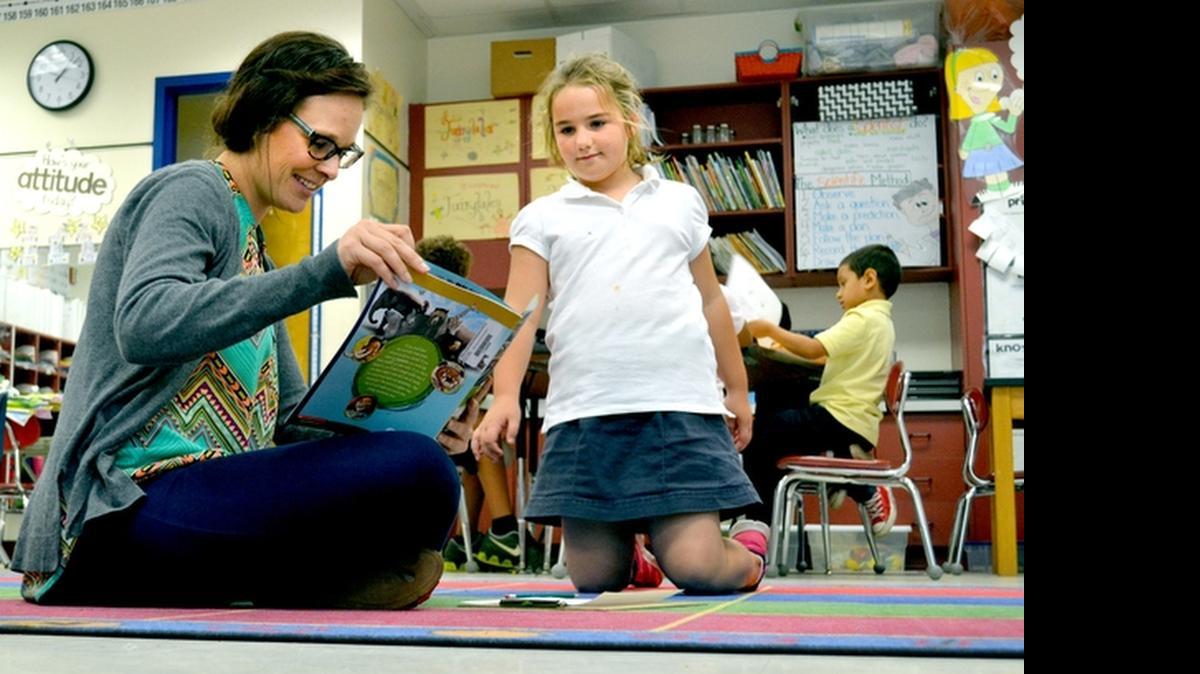 
A first grade teacher at Hilton Head Island Elementary School, Katelyn Roberts reads a book about animal teeth with one of her students, Catherine Whitaker, on May 21, 2015. Shortly after class ended that day, Roberts began packing up her classroom to move back to Ohio, and a lower cost of living. 

