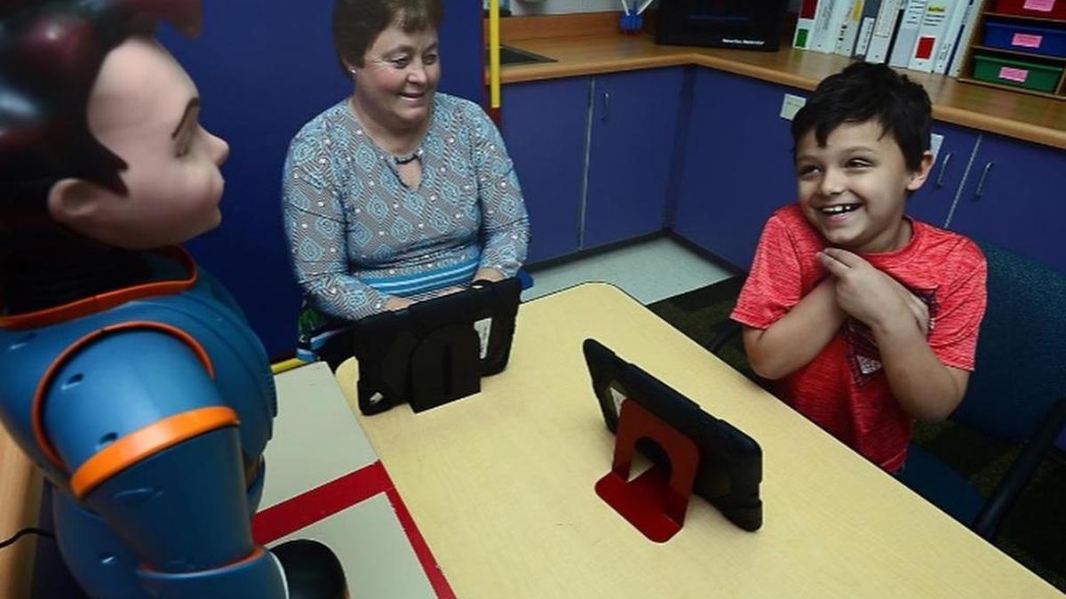Kim Speer, a McCarthy Teszler School autism specialist, works with Chris Pruitt, 8, on recognizing emotion in others with help from Milo, a robot designed for autistic students.