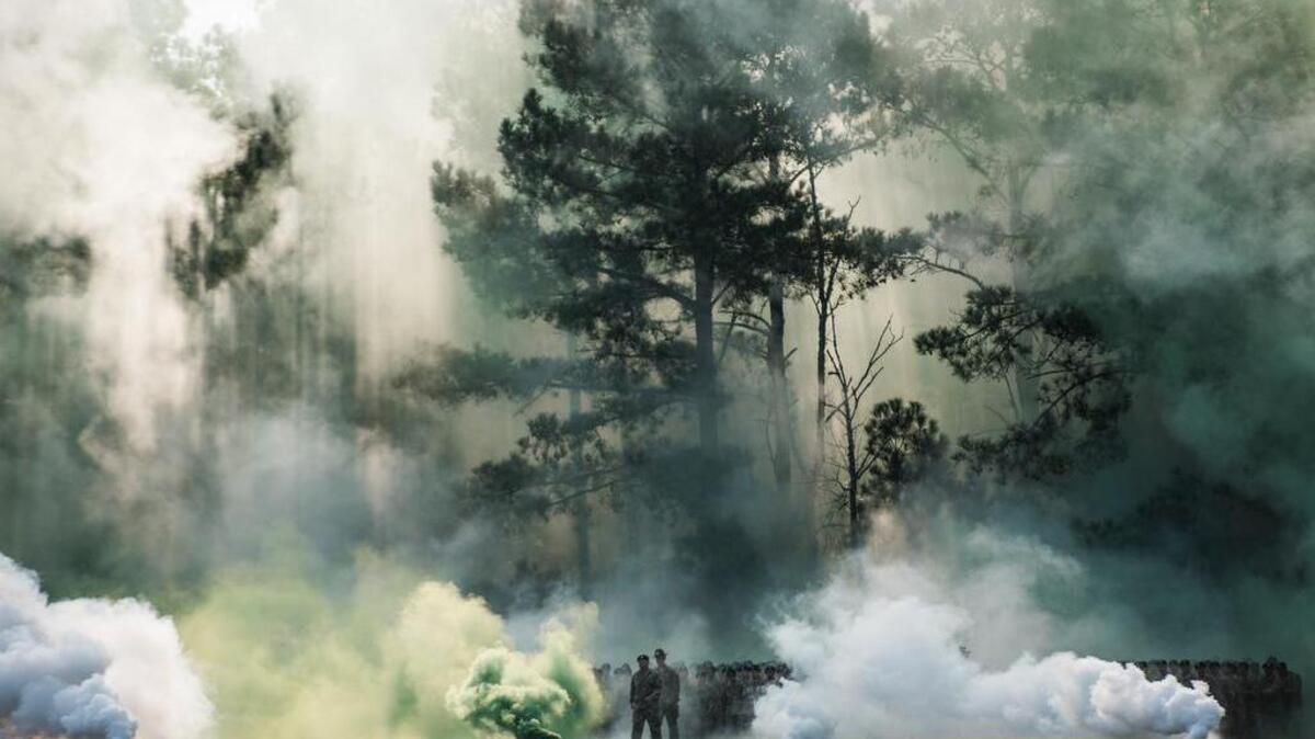 As relatives wait in the bleachers at Hilton Field on Family Day, soldiers emerge through smoke from a distant treeline. Family Day is the first time soldiers see their families since the start of basic training.