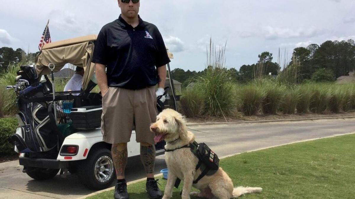 Justin Madore stands with his service dog, Cody, a 6-year-old Labradoodle, at Hampton Hall Golf Club on Monday, May 16, 2016, during the Wounded Heroes Golf Classic charity event.