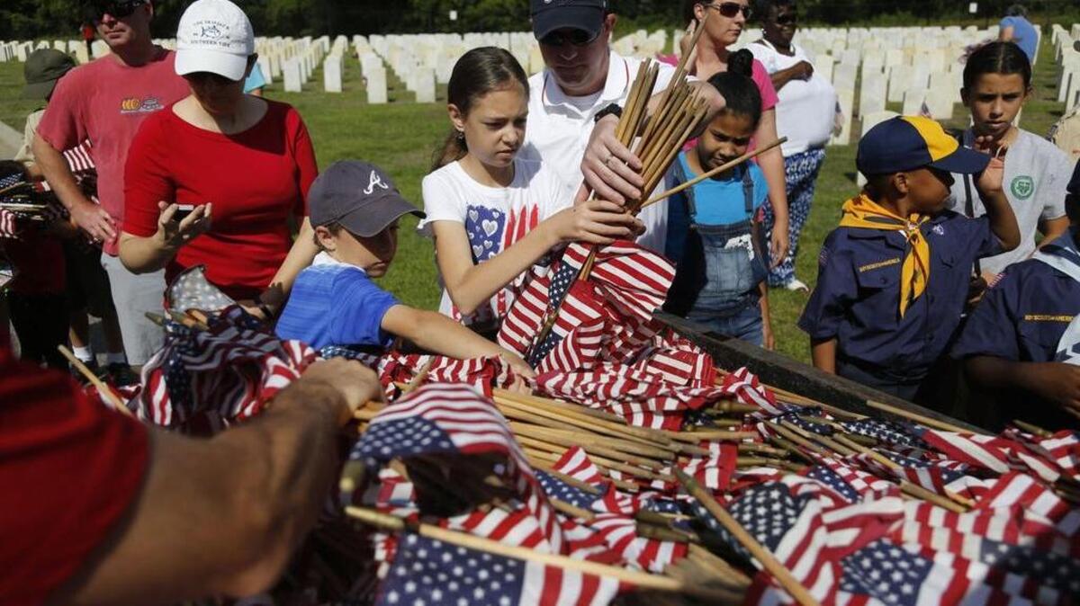 AnnaGrace Welch and Steve Welch, center, grab flags to place at markers in the Florence National Cemetery.