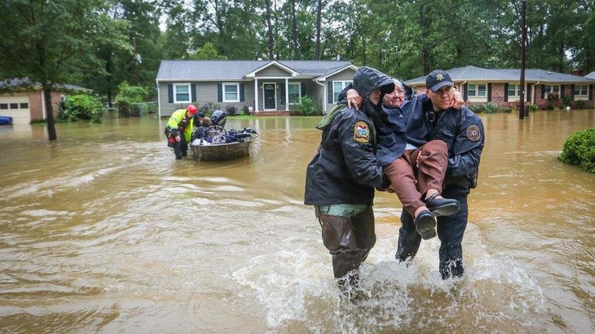 On October 5, 2015, DNR officer Brett Irvin and Lexington Co. Deputy Dan Rusinyak carry June Loch to dry land after she was rescued from her home in the Pine Glen subdivision off of Tram road in the St. Andrews area of Columbia.