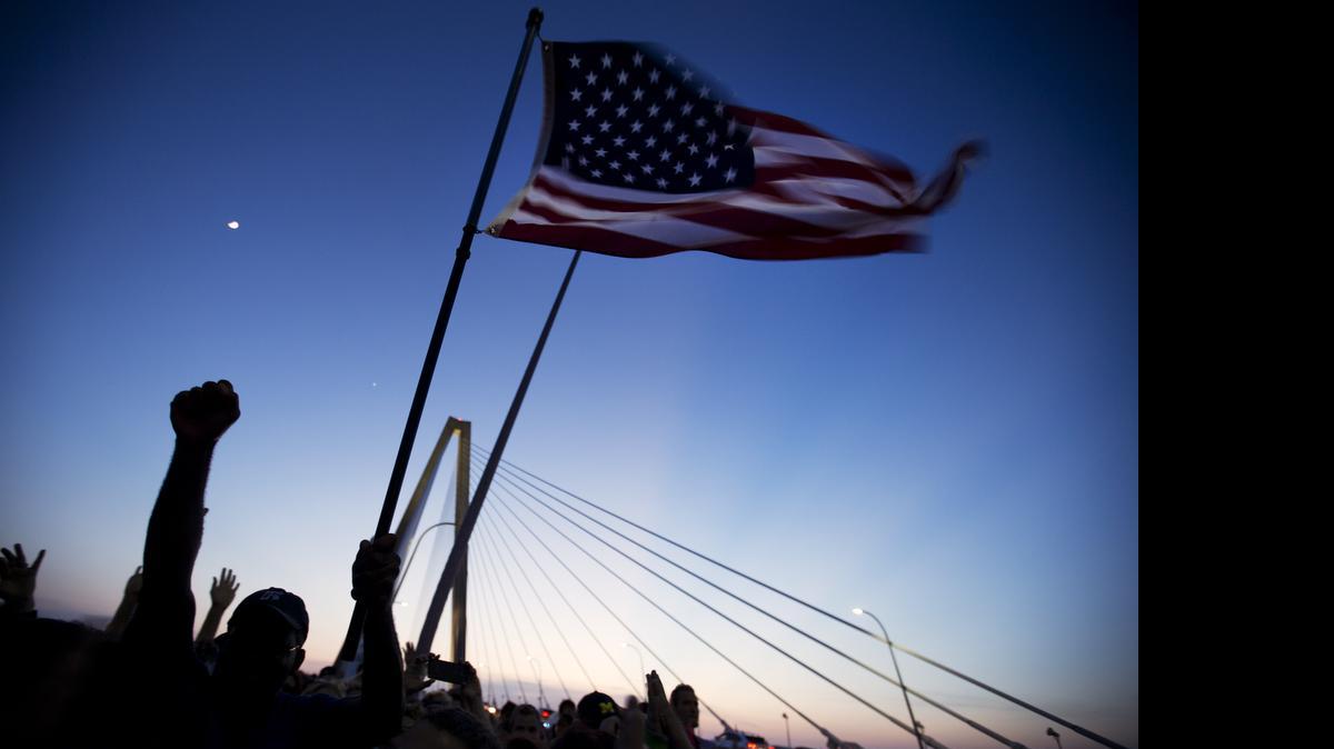 
People walk with an American flag as thousands march on Charleston's main bridge in a show of unity after nine black church parishioners were gunned down during a Bible study, Sunday, June 21, 2015, in Charleston, S.C. 
