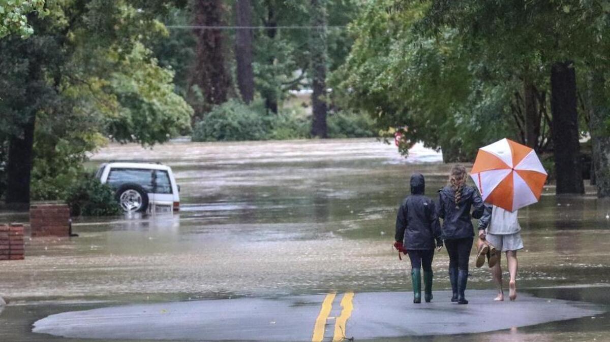 Onlookers walked down a flooded Woodlake Drive near Lake Katherine in the immediate aftermath of historic flooding.
