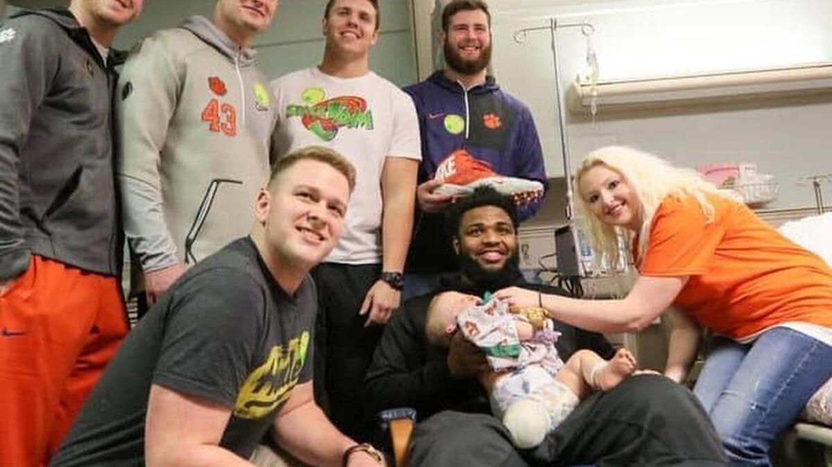 Clemson football players, from left, Austin Spence, Chad Smith, Daniel Funderburk, Isaac Moorhouse, Sean Pollard, stand near teammate Christian Wilkins holding one-year old Hudson Belviso of Spartanburg, near his mother Kaci Belviso, on Thursday at the Shriners Hospitals for Children in Greenville.