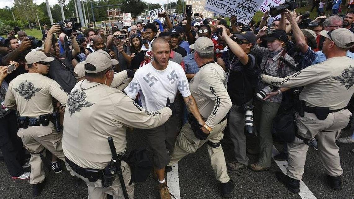 Randy Furniss, of Idaho, wearing a shirt with swastikas, is pulled through the line of Florida Highway Patrol officers for his safety after an angry mob followed him off the University of Florida campus in Gainesville, Fla., where white nationalist Richard Spencer spoke on Thursday, Oct. 19, 2017.