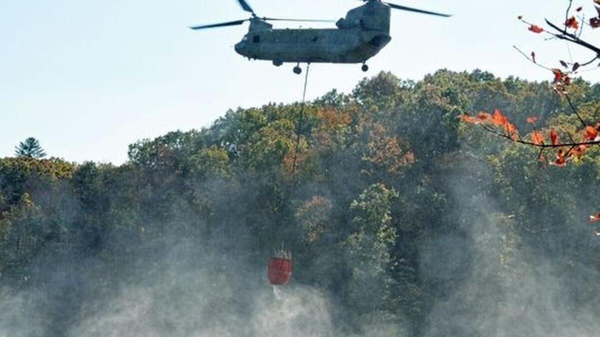 A helicopter lifts a bag with water to help firefighters contain the fire at Pinnacle Mountain