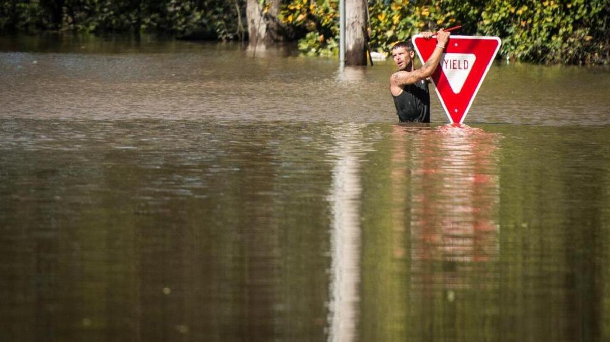 A man holds onto a yield sign after trying to swim out to help a stranded truck driver at NC 301 Highway and Tom Starling Road in Hope Mills (Cumberland County) on Sunday. Both people were rescued.