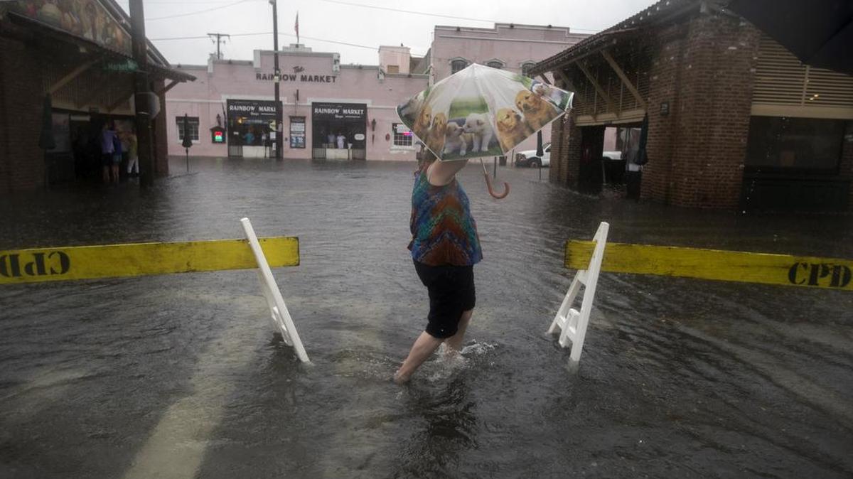 In this Thursday, Oct. 1, 2015 photo, a pedestrian walks past two barriers in place to stop vehicles from driving through the flooded streets of City Market in Charleston, S.C. Heavy thunderstorms can leave intersections impassable like the streets flooded near Charleston’s City Market area, a popular tourist haunt.