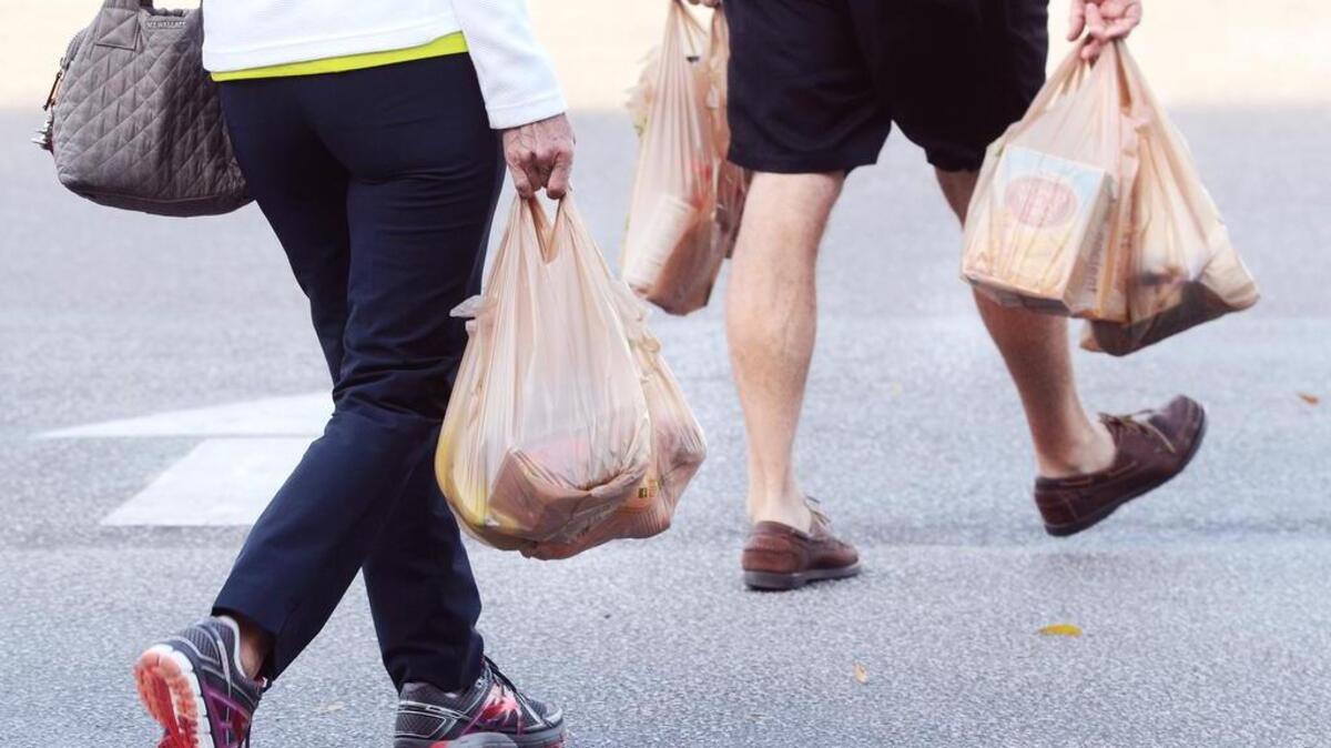 Shoppers leave the store with their groceries in plastic bags on Thursday.