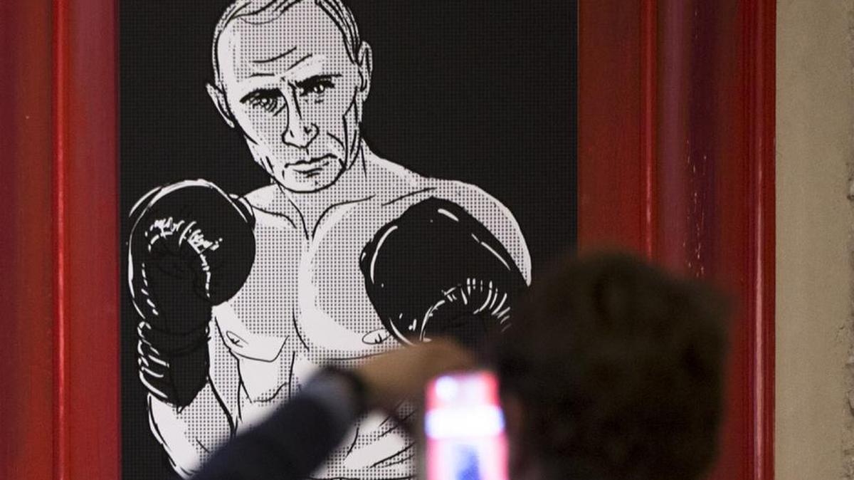 A man takes a picture of an artwork depicting Russian President Vladimir Putin as boxing legend Muhammad Ali.