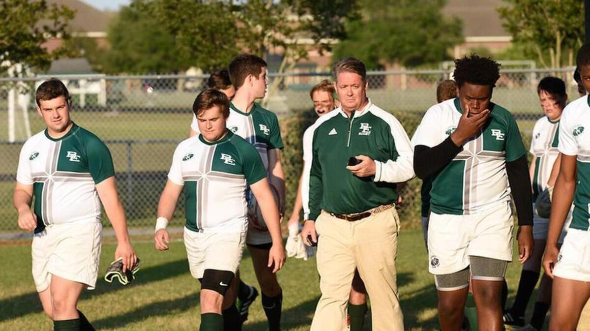 Bishop England assistant coach Baron Christopher Hanson leads players onto the pitch after a team prayer.