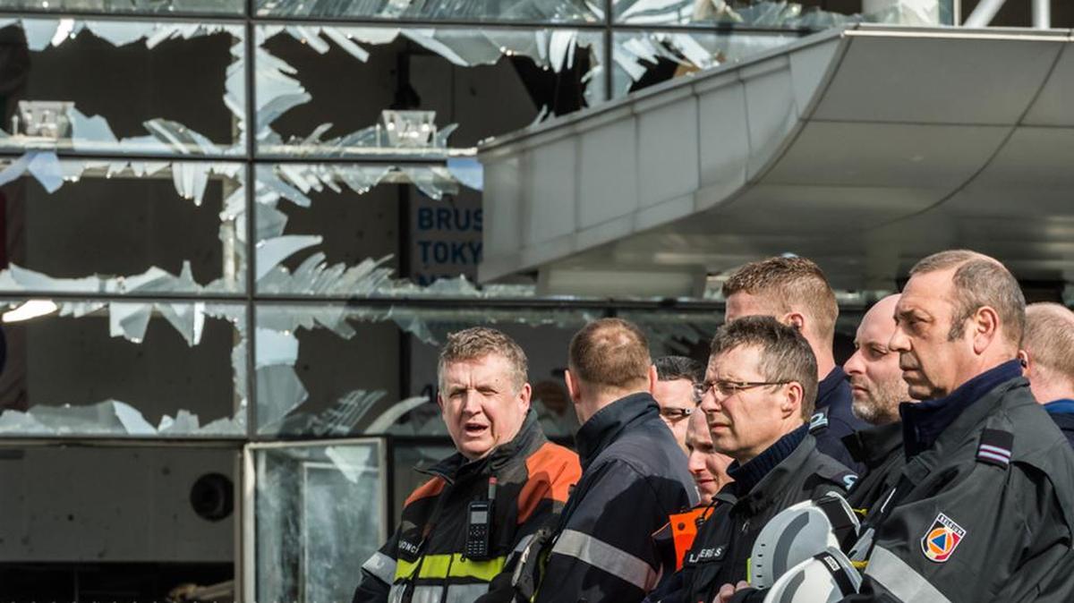 Firefighters and first responders stand next to blown-out windows at Zaventem Airport in Brussels on March 23, after terrorists attacked teh airport and a subway station.