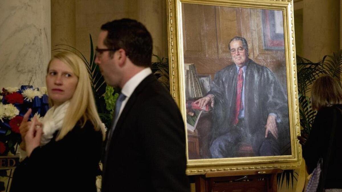 Members of the public walk past a portrait of late Supreme Court Justice Antonin Scalia in the Great Hall of the Supreme Court.