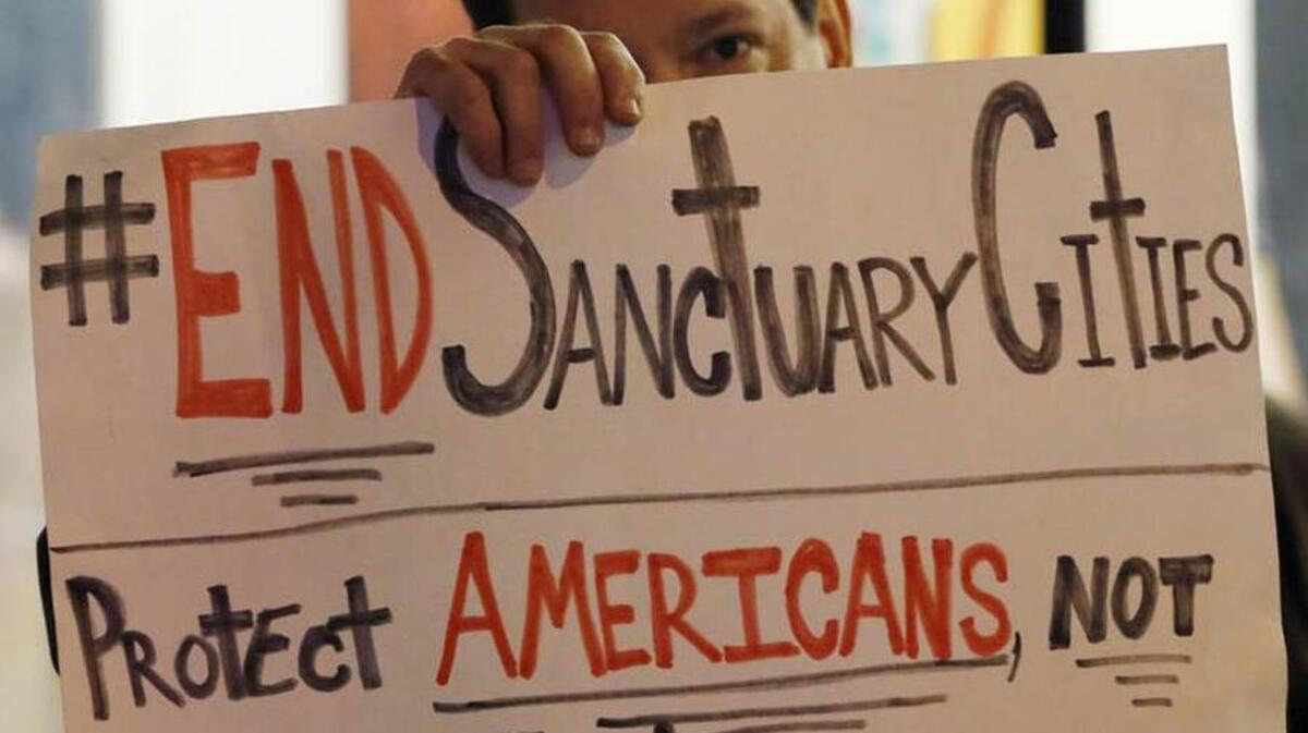 An anti-immigration protestor holds a sign in front of his face as he demonstrates in front of NBC Studios where a coalition of advocacy groups called for NBC to cancel the guest-host appearance of  Republican presidential candidate Donald Trump on this weekend’s “Saturday Night Live,” Wednesday, Nov. 4, 2015, in New York.  (AP Photo/Kathy Willens)