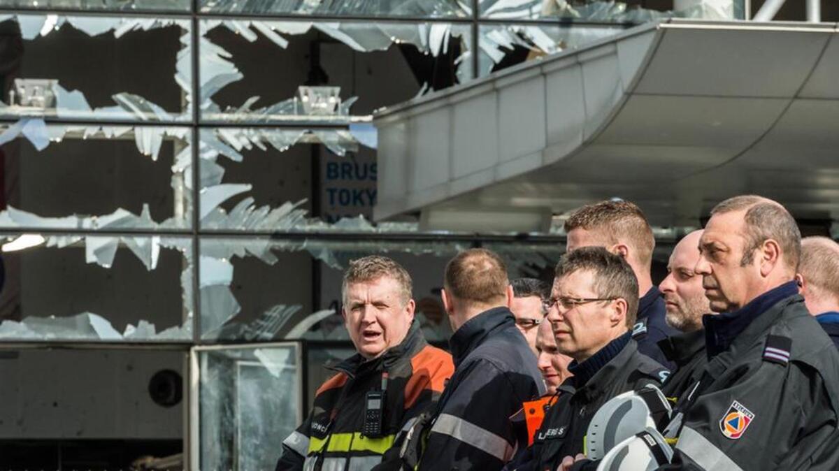 Firefighters and first responders stand next to blown out windows at Zaventem Airport in Brussels after the March terrorist attack.