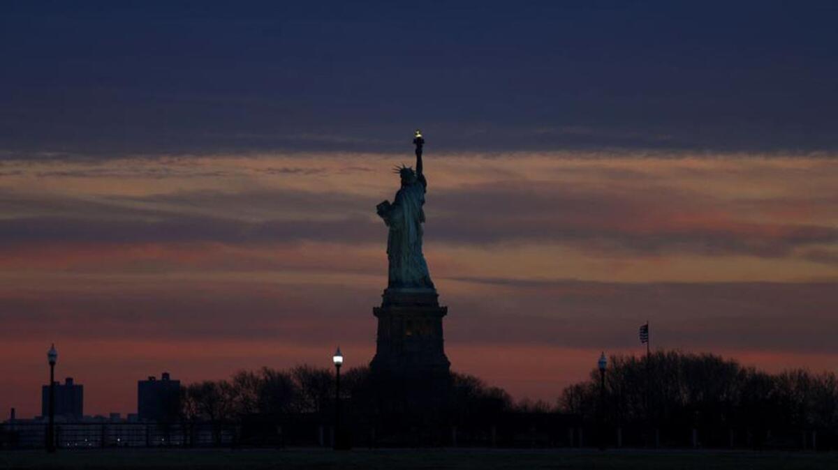 The setting sun lights up the sky over the Statue of Liberty viewed from Liberty State Park.