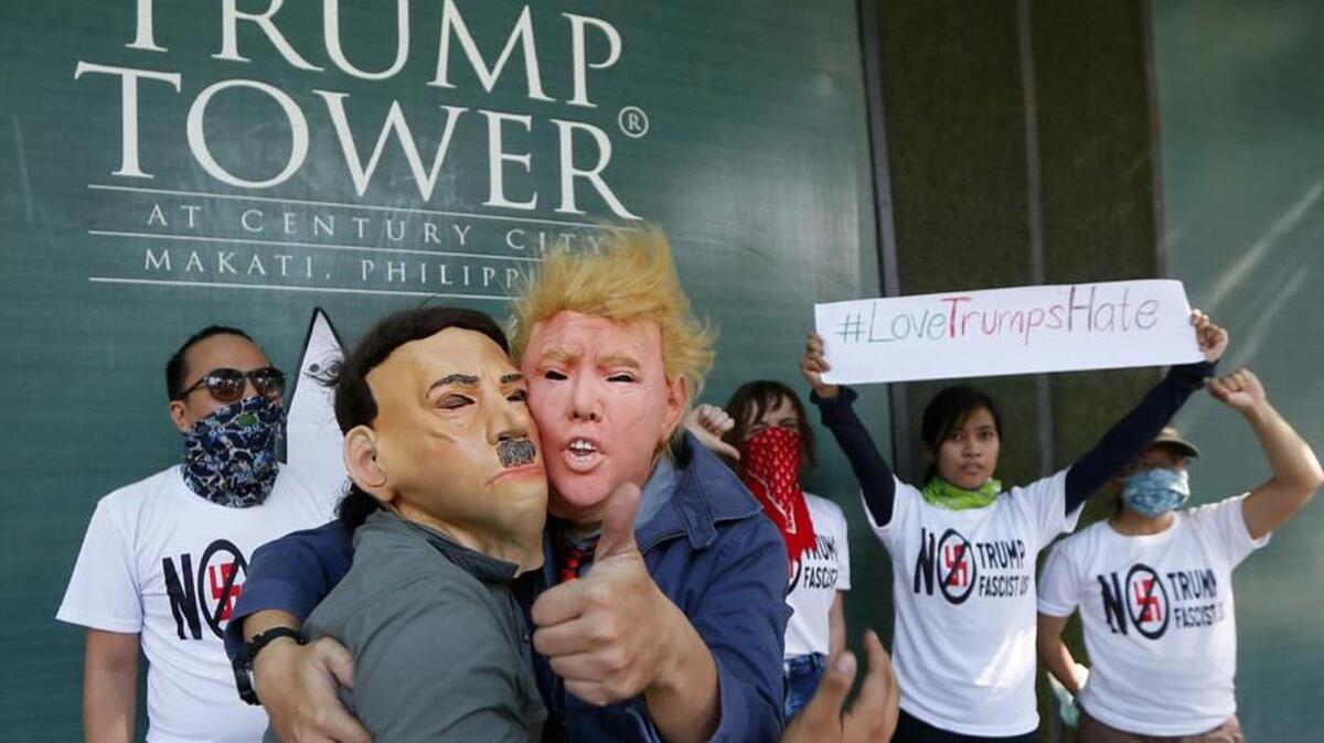 Protesters, one wearing a Donald Trump mask and another with an Adolf Hitler mask, embrace during a picket.